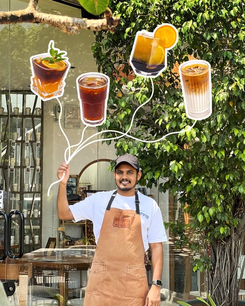 A barista holding a tray of iced coffee beverages with playful hand-drawn illustrations connecting the drinks to the server.