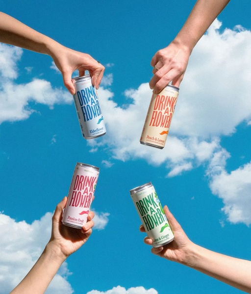 Four hands reach up to the bright blue sky, holding four different flavors of craft soda in a celebratory toast.