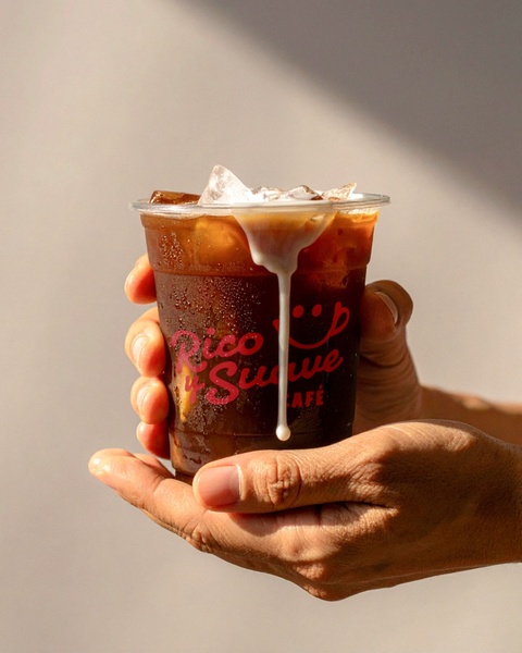 A close-up shot of a plastic cup filled with iced coffee, showing a fresh milk drip cascading down the side of the drink.
