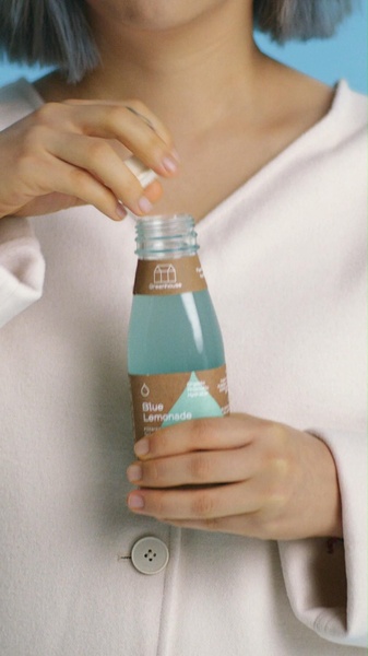 This creative features a close-up shot of a hand opening a bottle of blue lemonade, focusing on the product texture and packaging.