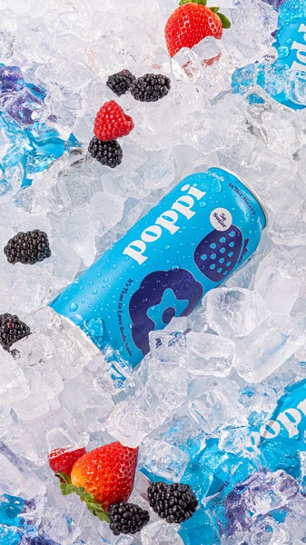 A vibrant 9:16 vertical shot featuring a can of Poppi wild berry soda nestled inside a bed of crushed ice, accompanied by fresh berries.