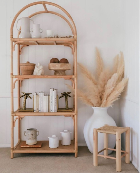 A high-quality, aspirational lifestyle shot featuring a curved rattan bookshelf styled with neutral home decor in a bright room.