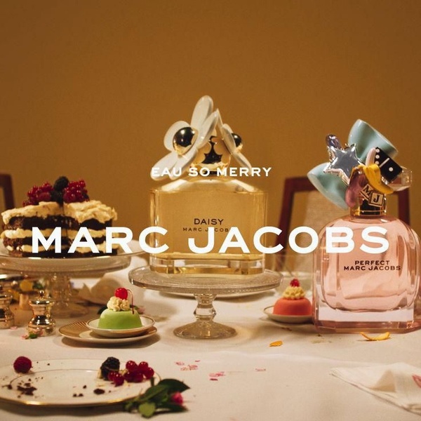 A sophisticated, warm-toned still life featuring luxury perfume bottles arranged on a dining table with desserts, using a soft, festive aesthetic.