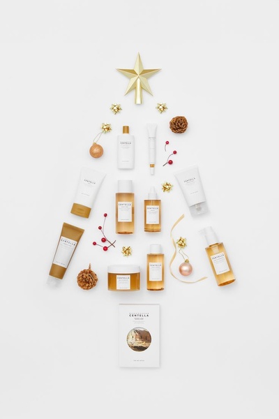 A top-down, balanced arrangement of skincare bottles and tubes forming a stylized Christmas tree on a clean, white background.