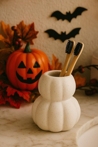 A clean, high-quality photograph of bamboo toothbrushes in a pumpkin-shaped holder next to a jack-o-lantern and bats, evoking a cozy Halloween atmosphere.