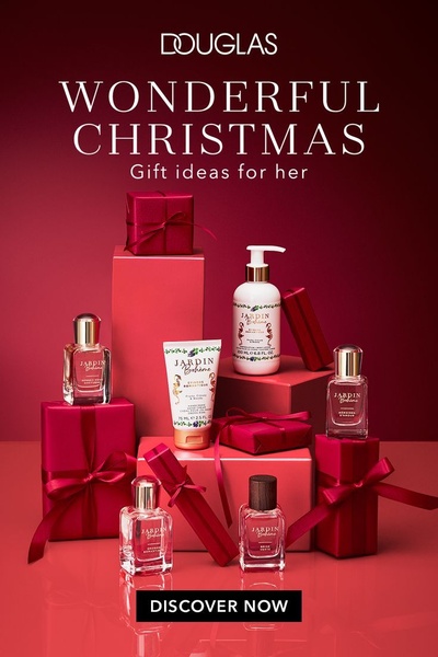 A high-end editorial display of various fragrance and skincare bottles arranged as gifts, utilizing a deep red color palette to evoke seasonal luxury.