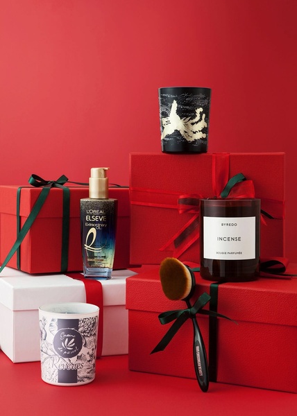 A refined product still life featuring luxury hair care and home fragrance items arranged with red gift boxes and green ribbons.