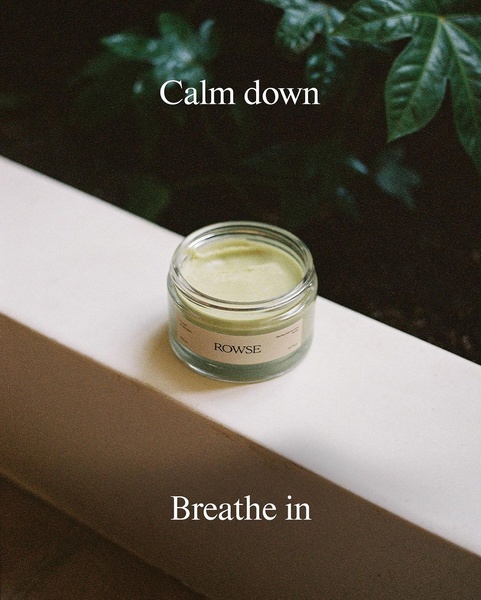 A close-up, serene product shot of a facial cream jar placed on a shelf against a dark, leafy background. The text overlay focuses on creating a sense of calm and breathing.