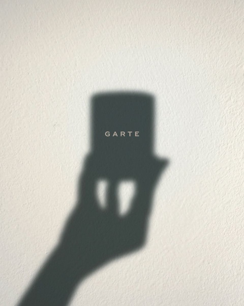 A high-contrast, minimalist photograph using a hand shadow to frame a skincare jar, emphasizing clean lines and brand recognition.