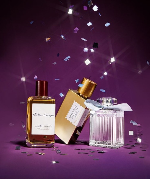 A high-end studio shot of three distinct perfume bottles arranged on a deep purple surface with metallic confetti falling around them.