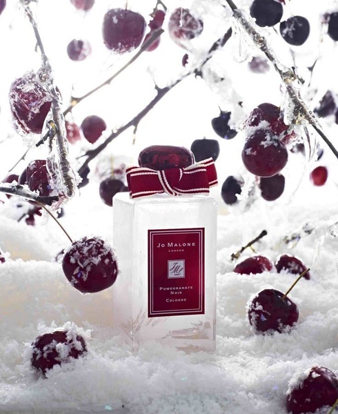 A high-end product shot featuring a cologne bottle surrounded by frosted cherries and snowy elements to evoke a wintry, sophisticated mood.