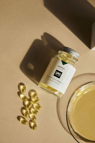 A high-end, clean product hero shot featuring a glass bottle of Omega 3-6-9 supplements alongside loose capsules and a pool of golden oil.