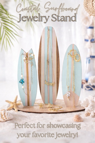 A high-quality product hero shot featuring a surfboard-themed jewelry stand displayed on a sandy beach setting, highlighting a coastal and organized lifestyle.