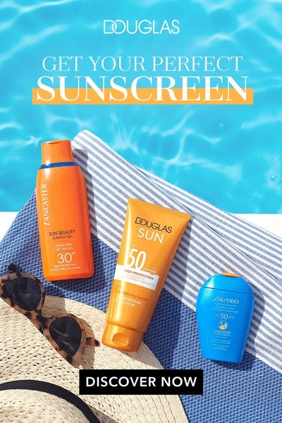 A top-down, high-angle product photograph featuring sunscreen bottles on a blue-and-white beach towel by a pool, accompanied by sunglasses and a straw hat.