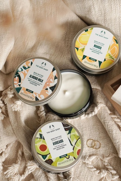 A high-angle top-down product shot featuring three open containers of nourishing body butter surrounded by textured fabric.