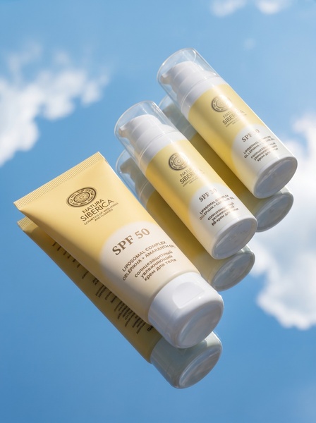 A high-quality product shot of sunscreen bottles placed on a mirror surface against a clear blue sky, emphasizing brand purity and natural light.