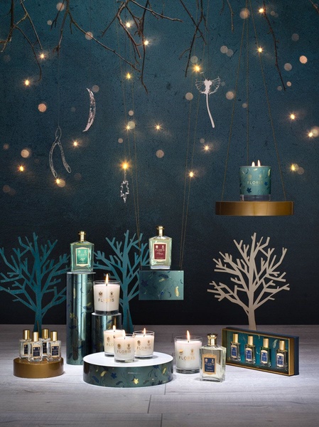 A sophisticated, high-end product display featuring multiple scented candles and perfume bottles arranged with fairy lights and tree accents.