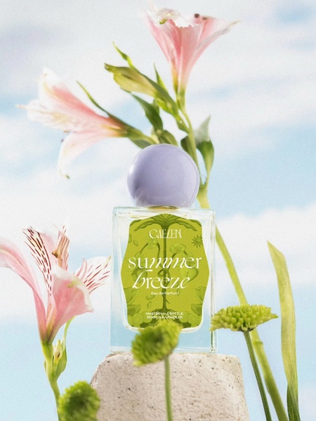 A high-quality studio shot of a perfume bottle nestled between spring flowers on a stone platform, capturing a soft and breezy aesthetic.