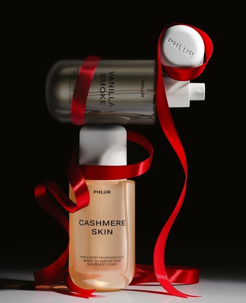 A high-end studio photograph showcasing two fragrance bottles stacked vertically, wrapped in a red silk ribbon against a pitch-black background.