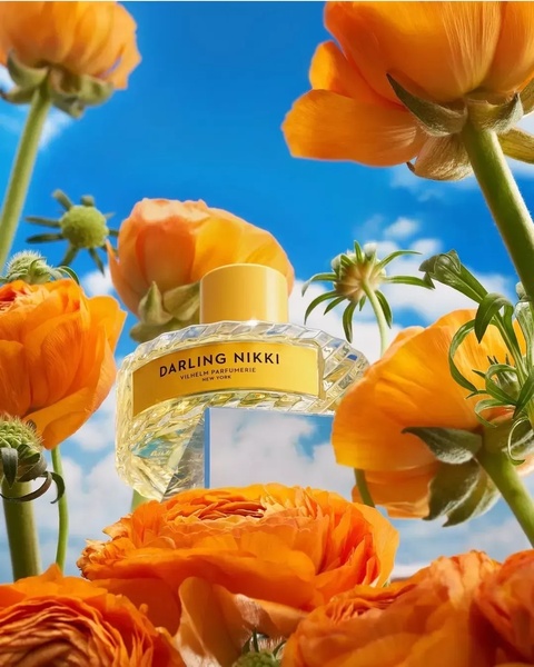 A high-end perfume bottle framed by vibrant orange flowers against a clear blue sky, emphasizing a premium and natural aesthetic.