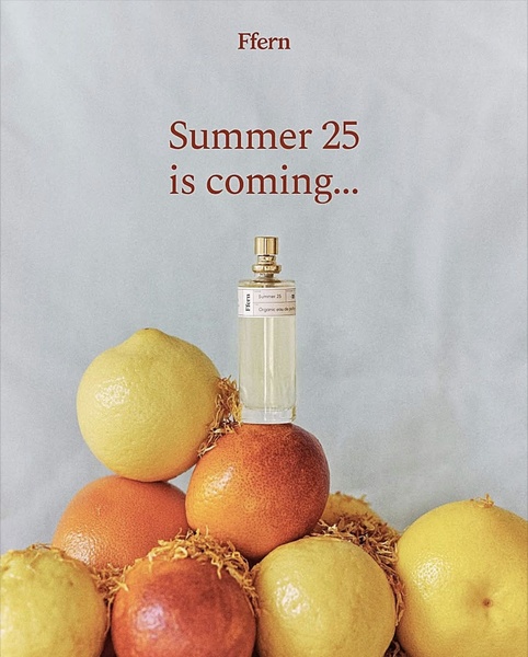 A clean, studio-lit shot of an organic eau de parfum bottle surrounded by fresh citrus fruits to evoke a bright, summer scent profile.