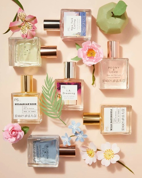 A high-angle studio shot featuring multiple perfume bottles arranged in a balanced grid, surrounded by minimalist floral and fruit elements.