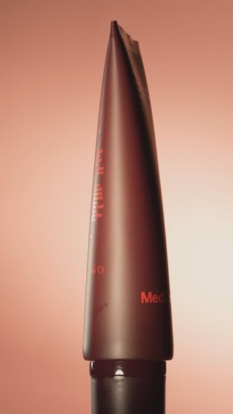 A close-up, high-contrast hero shot of a dark skincare tube set against a soft-focus warm backdrop to emphasize premium brand identity.