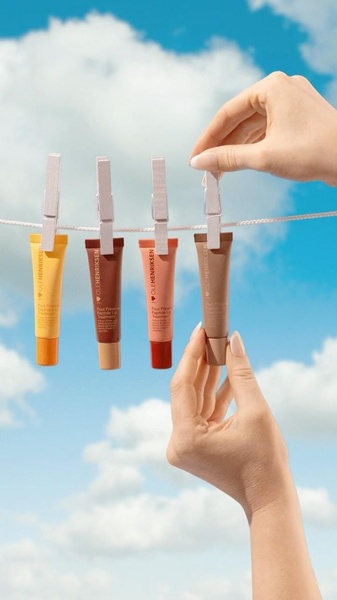 This creative showcases four tubes of lip treatment hanging on a clothesline against a bright blue sky, held by hands in a human-centric, playful composition.
