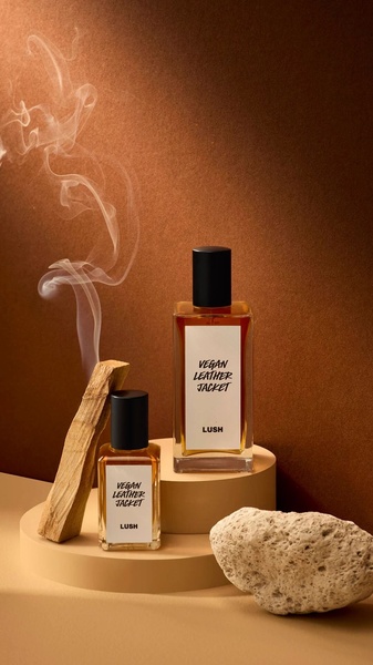 A high-end, studio-style product shot featuring two perfume bottles alongside palo santo wood and a natural stone against a warm, earthy gradient background.
