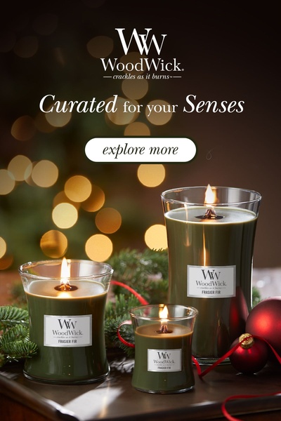 A high-quality product shot featuring three Frasier Fir candles of varying sizes, illuminated by soft bokeh holiday lights to create a warm, premium atmosphere.