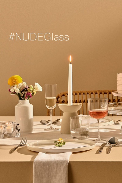 A refined, monochromatic table setting showcasing clear glassware, a burning candle, and simple floral accents under warm ambient lighting.