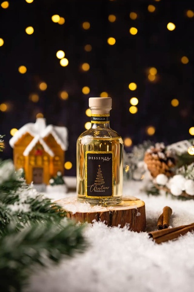A high-quality product hero shot featuring a fragrance bottle on a wooden base amidst Christmas decorations and soft bokeh lights.
