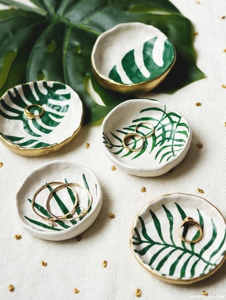 A high-angle lifestyle shot featuring artisanal ceramic trinket trays decorated with green leaf motifs, arranged on a textured white surface.