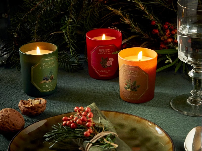This creative showcases three distinct scented candles in a warm, festive table setting, using rich colors and natural winter elements to evoke holiday emotions.