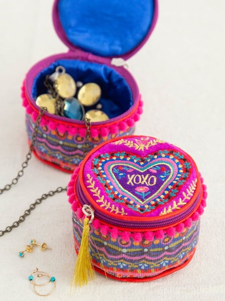 A close-up, high-contrast hero shot of two vibrant, embroidered circular jewelry cases, one open and one closed, arranged on a clean white surface with loose earrings.