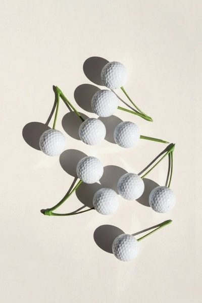 A high-concept, minimalist product image featuring golf balls arranged as cherries on a neutral background.