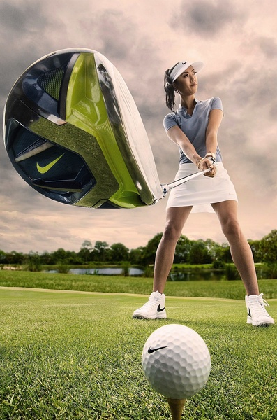 A close-up, wide-angle shot of a golf club driver emphasizing its size and technology, with a golfer positioned in the background on a green.