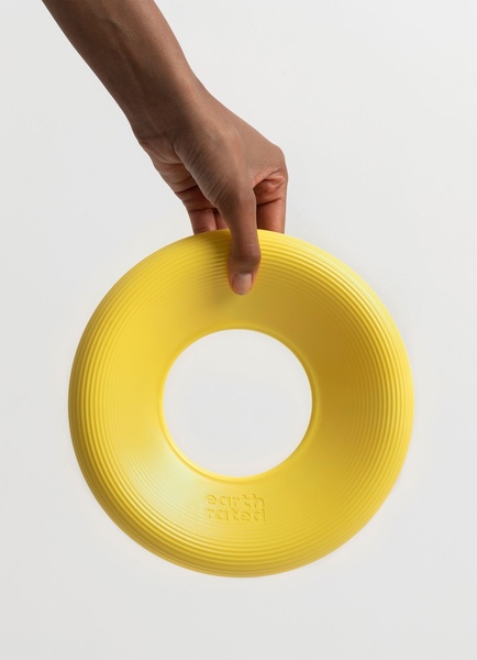 A high-contrast, minimalist studio photograph featuring a hand holding a bright yellow dog toy ring against a clean, neutral background.