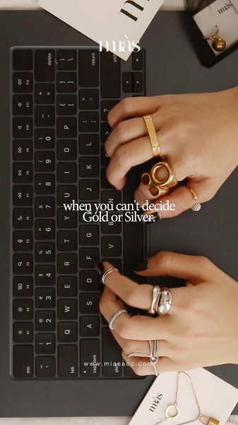 A close-up, first-person perspective video of someone wearing gold and silver rings while typing on a laptop, highlighting the relatable struggle of choosing between metals.