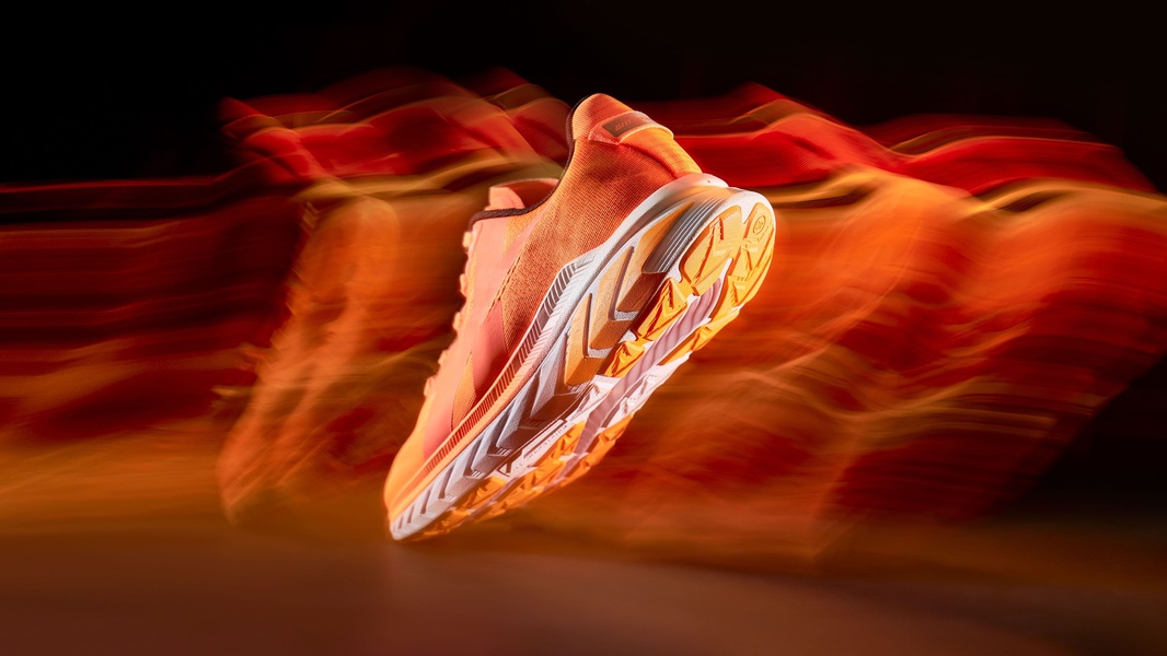 A high-performance running shoe is captured mid-air against a black background, utilizing intentional motion blur and vibrant orange hues to emphasize rapid movement.