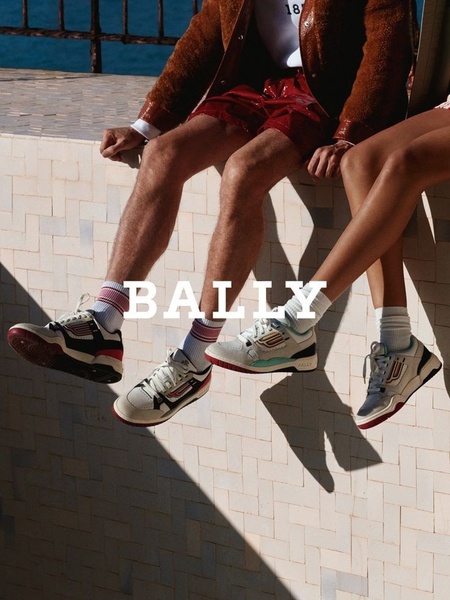 A high-angle, lifestyle-focused shot showing two people sitting on a ledge wearing matching casual sneakers, emphasizing the product in a relaxed, aesthetic environment.