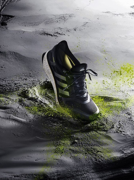 A high-performance running shoe positioned as if just striking the ground, surrounded by vibrant green dust particles to signify raw energy.
