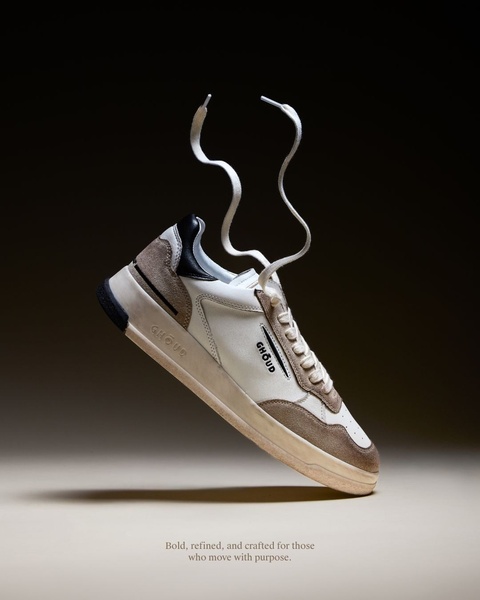 A studio-shot, vertical ad creative featuring a single sneaker suspended in mid-air with laces gracefully floating above it against a dark-to-light gradient background.