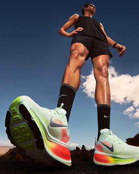 A low-angle, wide-shot perspective highlighting a running shoe by making it appear massive and impactful against a clear blue sky.