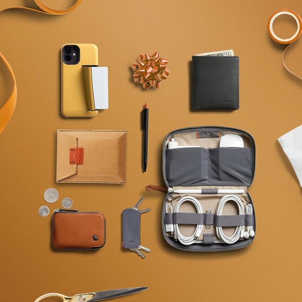An organized flatlay of daily carry items, including a phone, wallet, pens, and a tech organizer case, arranged on a flat warm-toned surface.