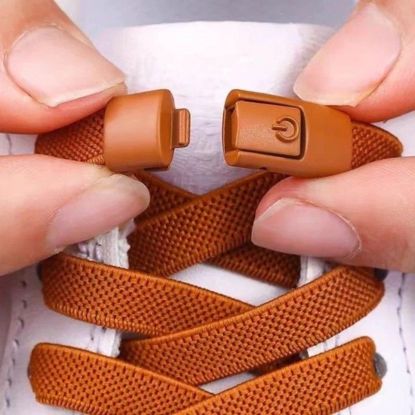 A high-contrast, macro-style shot showing fingers connecting a magnetic locking mechanism on brown elastic shoelaces.