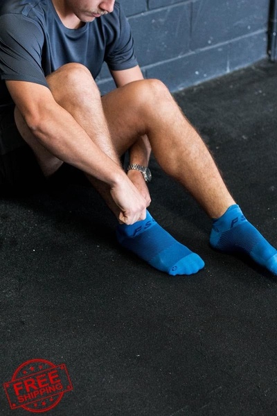 A close-up lifestyle shot of a person putting on performance ankle socks in a gym environment.