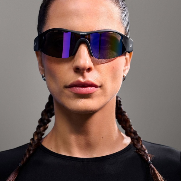 A close-up, centered portrait of an athlete wearing sleek, polarized sports sunglasses, emphasizing the frame design and lens finish.