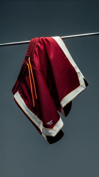 A high-quality studio shot of athletic shorts suspended on a metal rod against a clean, dark gray backdrop.