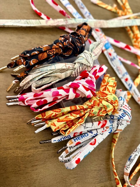 A high-angle, top-down shot displaying a variety of colorful custom shoelace designs spread across a wooden surface.